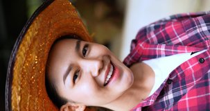 Cheerful Asian farmer woman wearing plaid shirt and jeans with straw hat is making online video call to explaining and introducing or live on social media in cattle farm