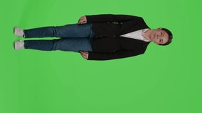 Vertical video: Front view of negative mad office worker showing disapproval on camera, acting angry and furious standing over full body greenscreen backdrop. Young woman expressing disagreement in