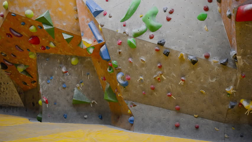 Athletic woman approaches climbing wall with artificial rocks. Professional climber trains moving to top of wall stepping on holds carefully backside view