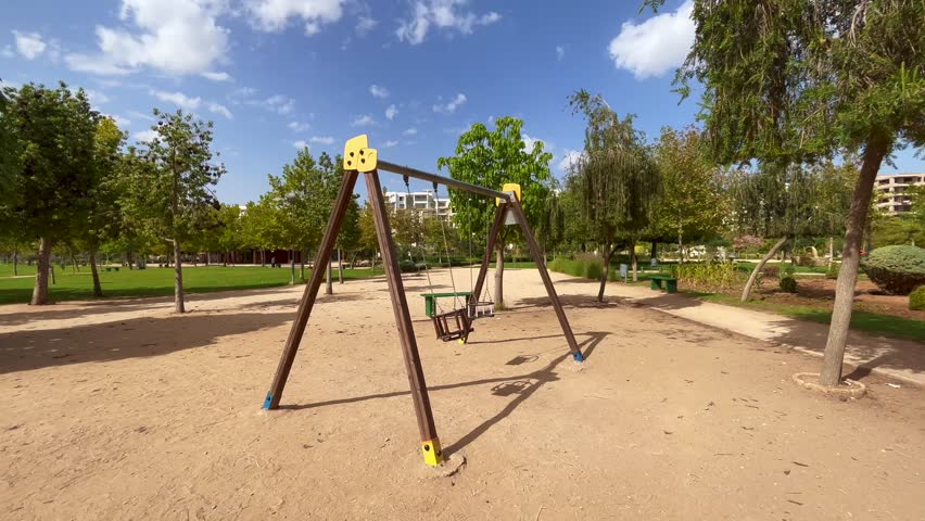 An empty swing in the park with trees in the background