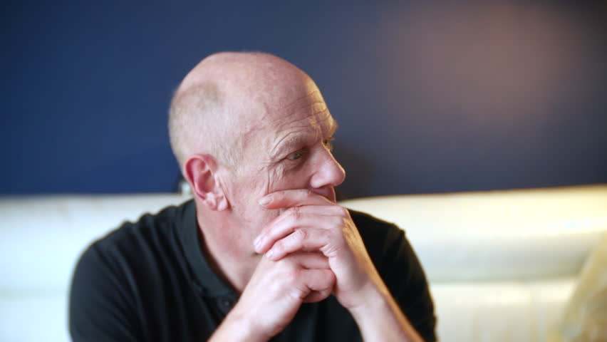 A mature senior man with mental health problems is sitting at home pensive looking lost and confused.