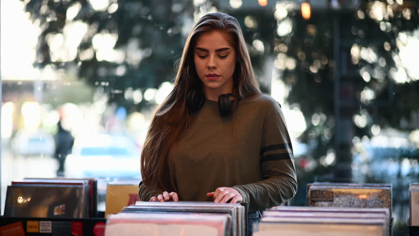 Young beautiful woman with headphones in a vinyl store choosing records. Vintage Vinyl LP In Records Shop. Vinyl record store, music, sale and shopping concept. Music lover.