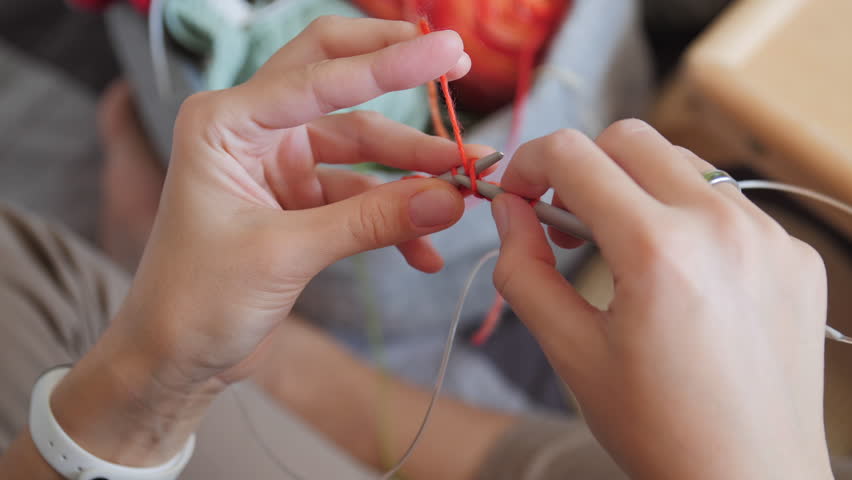 Close-up video of woman knitting something small. Anti-stress hobby. Tranquil leisure at home. Handicraft. Online lessons for amateurs on laptop.