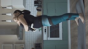 Vertical video. Sporty young mother is engaged with child in fitness exercises, woman doing squats in the kitchen