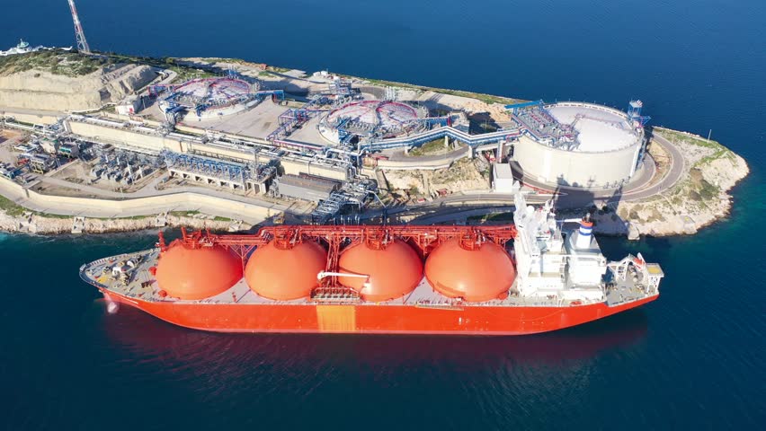 Aerial drone top down video of LNG (Liquified Natural Gas) tanker anchored in small gas terminal island with tanks for storage to store and regasify LNG Royalty-Free Stock Footage #1098235973