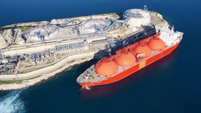 Aerial drone top down video of LNG (Liquified Natural Gas) tanker anchored in small gas terminal island with tanks for storage to store and regasify LNG