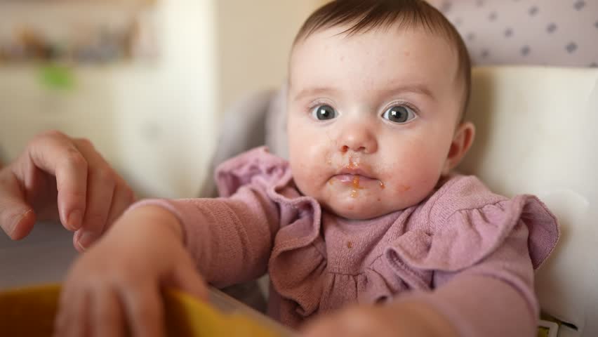 baby newborn eats. dirty mess baby girl eating vegetables. baby daughter eats on a feeding chair dirty face. naughty dirty babe indulges while feeding. happy kid dream indoors family weaning concept