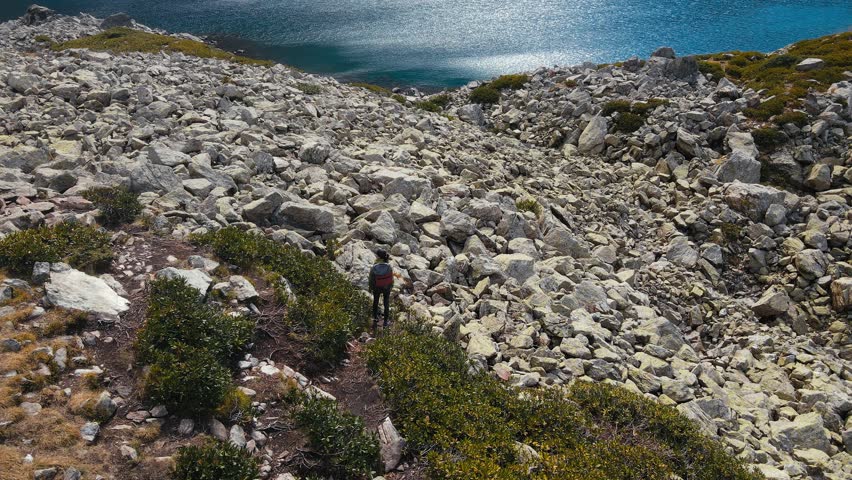 Female traveler walking rocky trail around mountain lake, aerial view