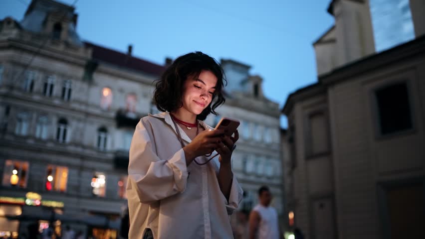 Smiling woman using smartphone on street with night city lights on background Royalty-Free Stock Footage #1098239855