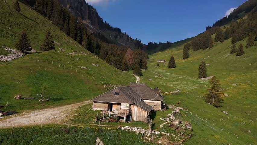 Aerial, male backpacker walking towards rural cabin by the mountains during summer