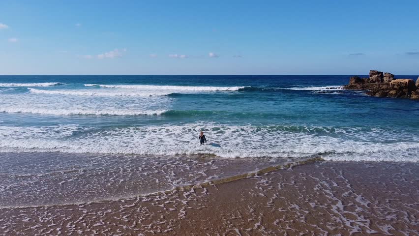 A girl entering in the water to start to surf on a beach in the Algarve, Portugal.