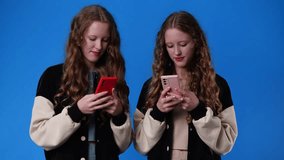 4k video of twin girls using their phones on blue background.