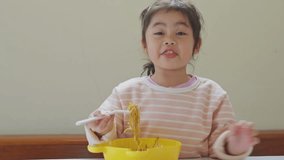 Asian baby girl enjoy happy using cutlery spoon and fork eating delicious noodle in kitchen on dining table. Happy asian baby girl practice eating by her self on dining table. Video footage 4K.