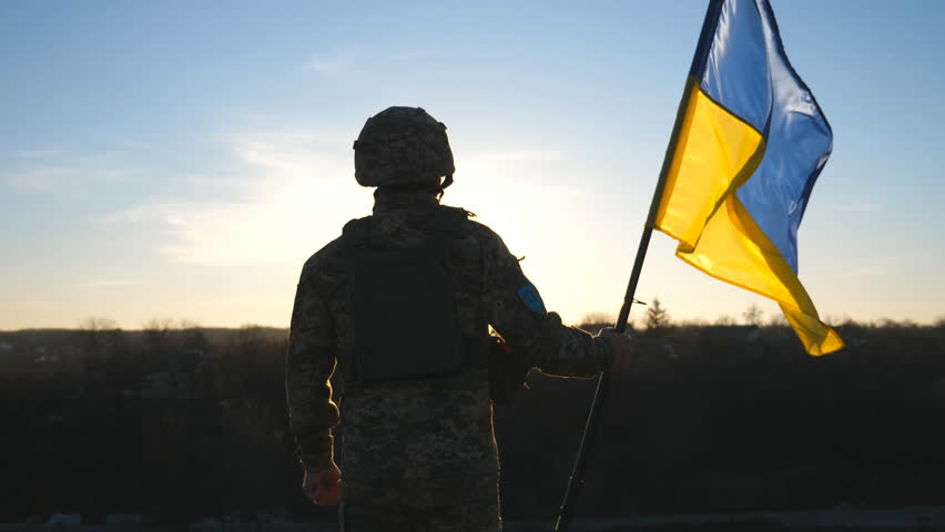 Soldier of ukrainian army holding waving flag of Ukraine against background sunset. Man in military uniform and helmet lifted up flag. Victory against russian aggression. Invasion resistance concept | Shutterstock HD Video #1098249837