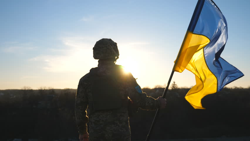 Soldier of ukrainian army holding waving flag of Ukraine against background sunset. Man in military uniform and helmet lifted up flag. Victory against russian aggression. Invasion resistance concept | Shutterstock HD Video #1098249837