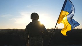 Soldier of ukrainian army holding waving flag of Ukraine against background sunset. Man in military uniform and helmet lifted up flag. Victory against russian aggression. Invasion resistance concept - Powered by Shutterstock - Get 15% off with code: PIKWIZARD15