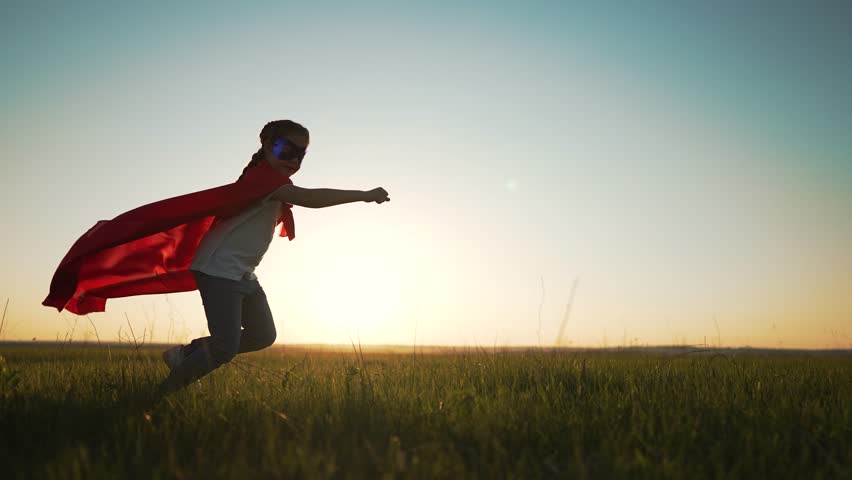 Happy child girl in superhero costume in the park. A girl in a mask runs through the grass in a field at sunset. Concept of success and victory. Dream girl is actively playing in the park outdoors. | Shutterstock HD Video #1098251603