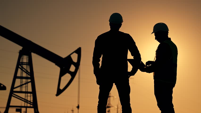 Teamwork. Two workers in hard hats at sunset. Working oil pump silhouette. Two engineers work on an oil pump at sunset. Extraction of crude oil minerals. Field of oil resources production of gasoline
