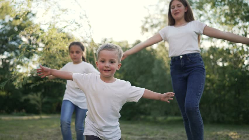 happy children run on grass with arms to sides. Cheerful children play plane pilot in park. Smile on children faces. Family on picnic in nature. Son and daughters play running on the grass in the park Royalty-Free Stock Footage #1098251647