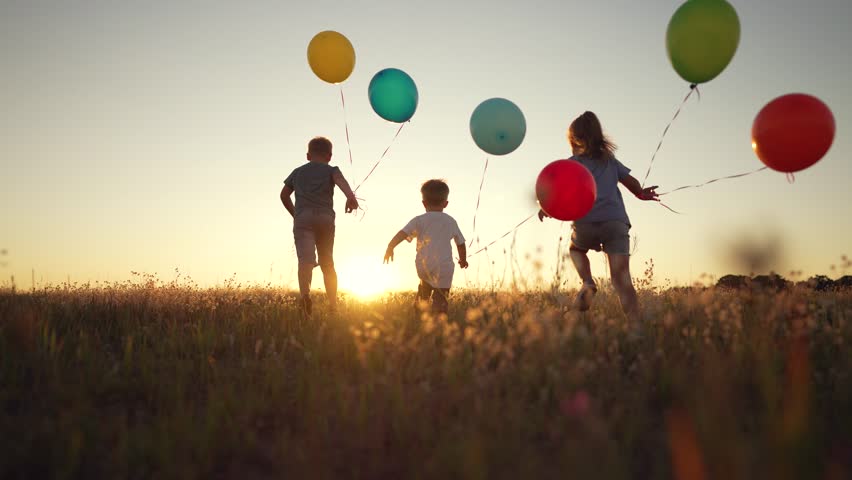Happy children with balloons. Family run together on the green grass in nature. Children with a smile on their faces play together in the park. Family running in the park at sunset with balloons Royalty-Free Stock Footage #1098251675