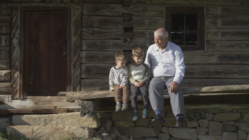 Elderly man and two children on wooden porch of the rustic house