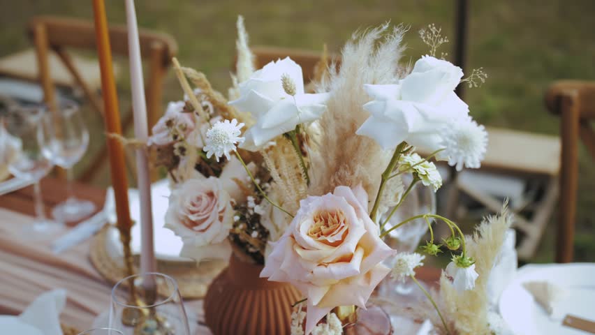 Close-up beautiful bouquet of roses and dried flowers on the table served and decorated with candles in boho style wedding dinner, plates and wine glasses, no people shot, slow motion. | Shutterstock HD Video #1098253189