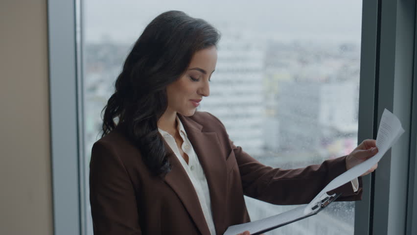 Young successful woman boss reading contract standing at office window in elegant suit closeup. Portrait of attractive businesswoman manager feeling happy looking papers with company financial results | Shutterstock HD Video #1098253677