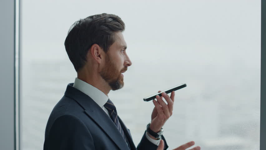 Angry middle-aged ceo manager calling smartphone gesturing emotionally standing at office window closeup. Stressed business man dissatisfied company work. Bearded entrepreneur using mobile phone. | Shutterstock HD Video #1098253687