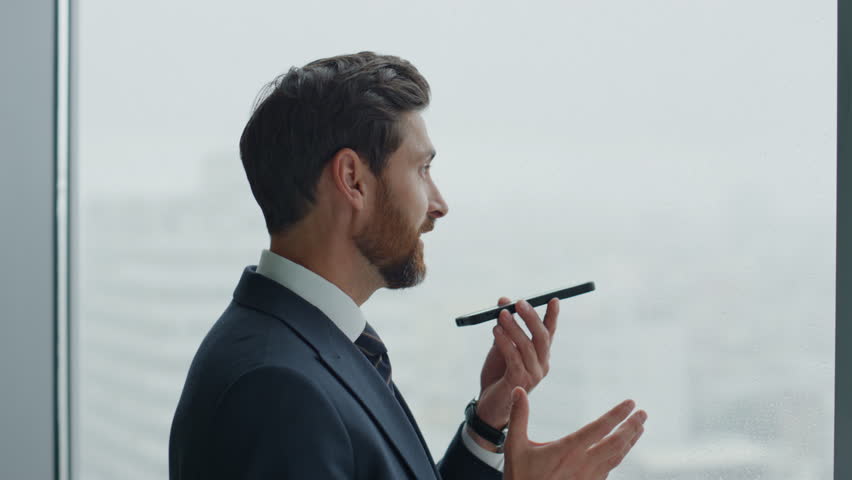 Bearded attractive middle-aged man talking phone at office using dynamic close up. Elegant businessman negotiate virtual conversation on smartphone standing near window. Professional communication. | Shutterstock HD Video #1098253691