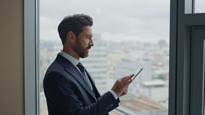 Successful confident boss holding tablet rejoicing company achievement reading financial report close up. Attractive bearded business man feeling happy standing with tab computer near office window. Royalty-Free Stock Footage #1098253723