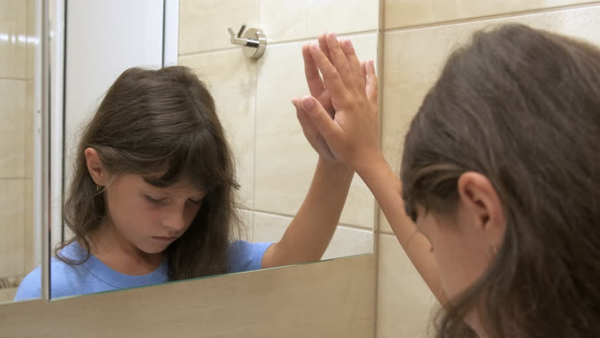 Child depression. Lonely little girl looks in the mirror in the bathroom.