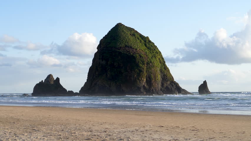 Haystack Rock Sea Stack at Cannon Beach Oregon with sandy shoreline, calm waves, and cloudy sky