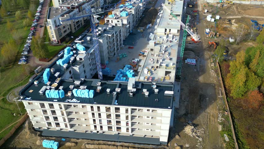Flying over construction site. Top view of yellow tower cranes mounted on crane rails. A foreman in a helmet is walking among building materials. Excavators are preparing a new site for foundation. | Shutterstock HD Video #1098259097