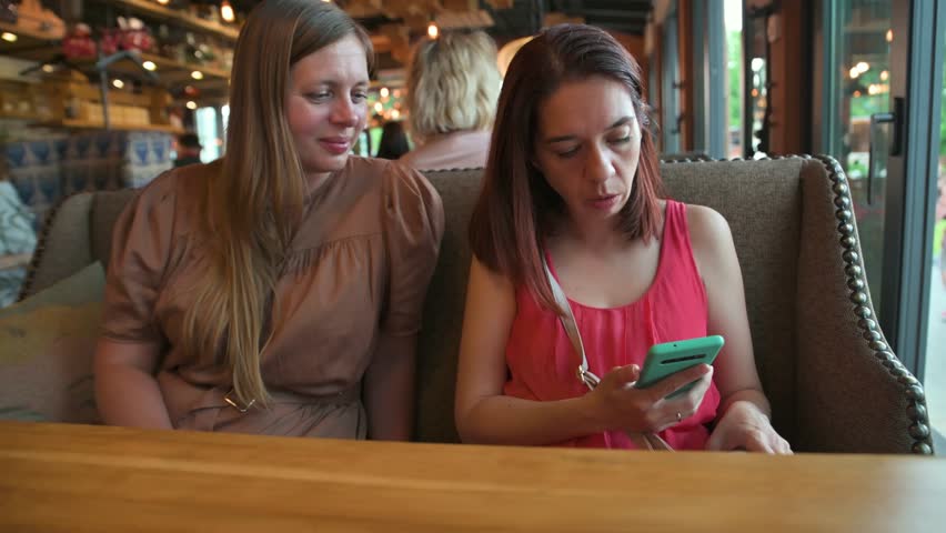 Women talking in restaurant via smartphone. 4k video footage in slow motion