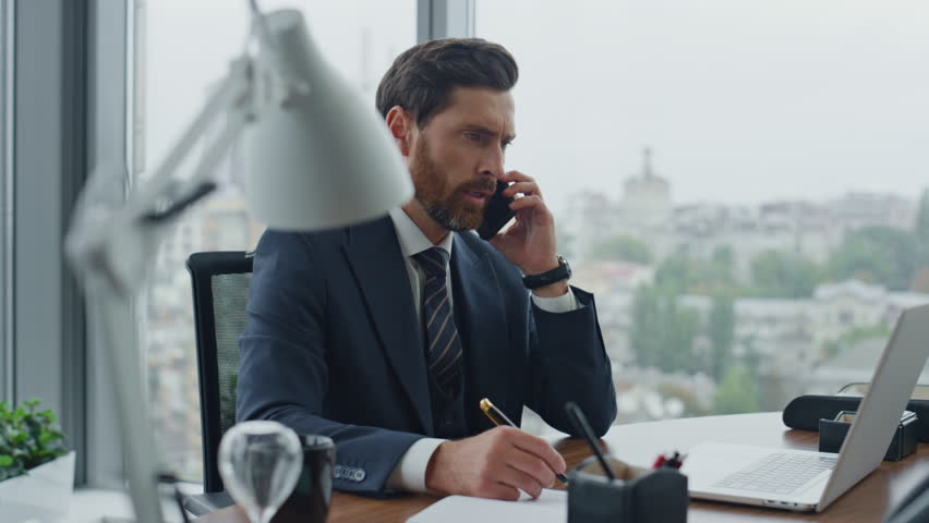 Annoyed director arguing on phone call sitting office desk with laptop close up. Nervous bearded businessman talking loudly on smartphone feeling dissatisfied company work. Man manager shouting mobile | Shutterstock HD Video #1098268199