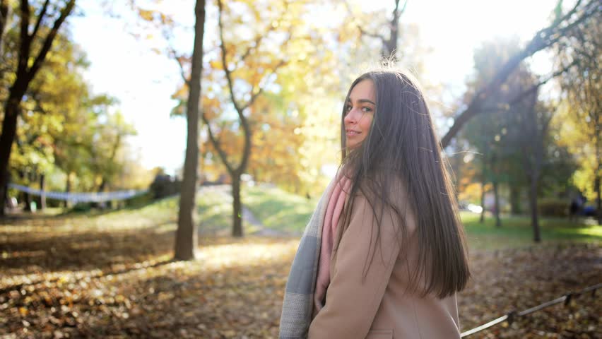 Side view portrait of caucasian beautiful young woman going forward in park with glass of coffee and drinking it. Walk in autumn park against nature landscape with trees and yellow-gold fallen leaves. Royalty-Free Stock Footage #1098273633