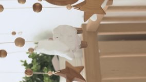 Vertical video. Close-up of cute hanging mobile with wooden toys rotating on the crib in nursery