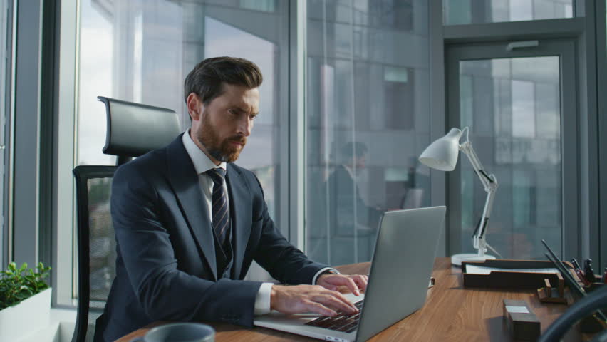 Thoughtful bearded office worker turning off laptop closing lid at desk in modern office. Focused business man completing work at computer getting up to panoramic window. Serious boss looking outside. Royalty-Free Stock Footage #1098288497
