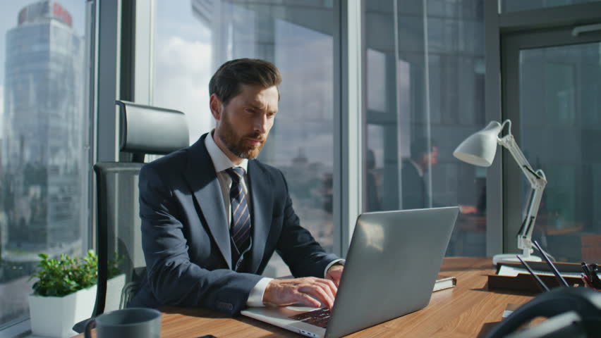 Confident bearded business man finish laptop work shutting notebook lid. Stylish manager getting up from wooden desk taking break. Serious boss looking on panoramic window modern office at skyscraper. Royalty-Free Stock Footage #1098288565