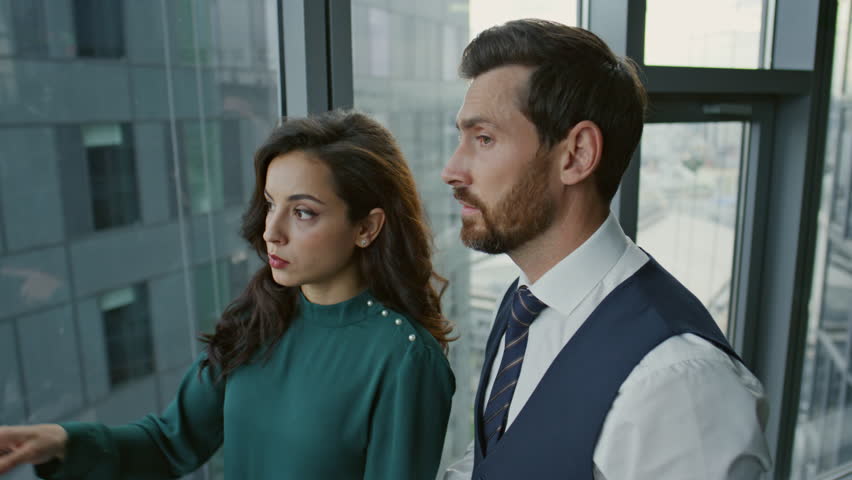Business colleagues talking about company issues in modern office close up. Confident couple businesspeople discussing work project standing panoramic window. Focused office mates working together