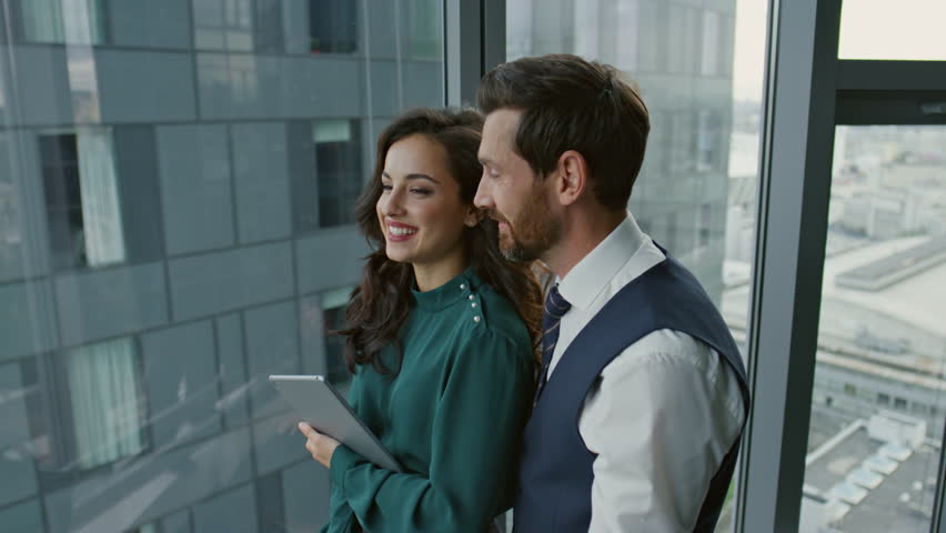 Cheerful couple businesspeople have casual conversation after meeting in company office near panoramic window close up. Smiling colleagues talking joyfully at work break. Happy team have fun together.