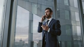 Worried ceo calling phone standing near office window close up. Confident bearded executive manager have serious telephone conversation feeling stress. Busy nervous business man finish smartphone talk - Powered by Shutterstock - Get 15% off with code: PIKWIZARD15