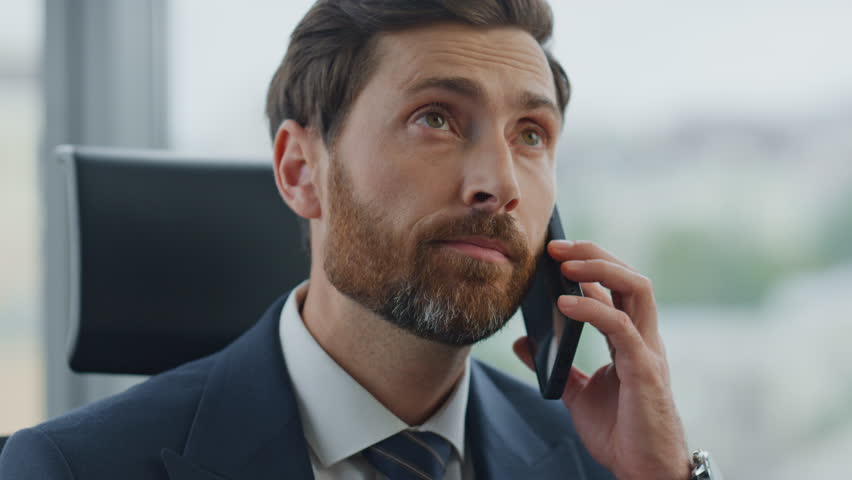 Tired bearded office manager talking smartphone hearing bad news closeup. Serious company employee listening client complaints at phone conversation. Business man looking disappointed feeling stressed | Shutterstock HD Video #1098288649