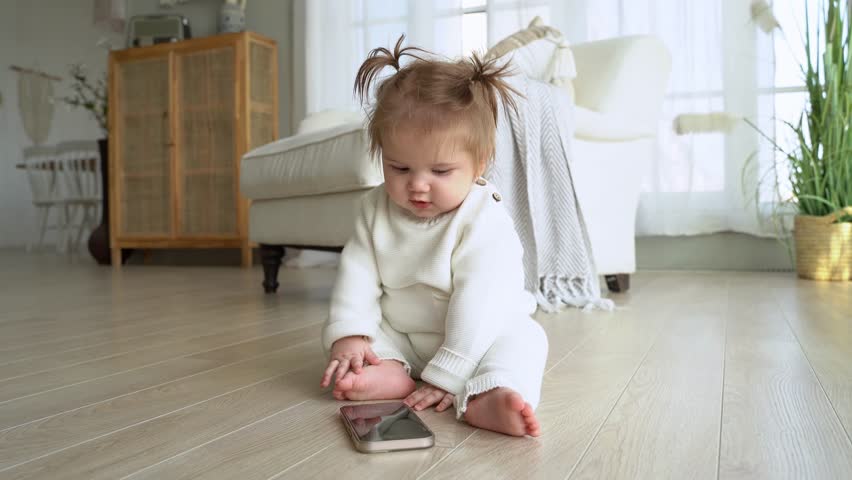 Baby playing with parent smartphone while sitting on floor in living room. | Shutterstock HD Video #1098292039