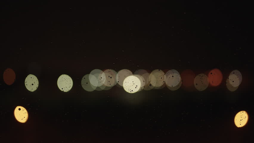 Night backdrop closeup shot of rain drops sliding on glass window with bokeh blurre lights on background