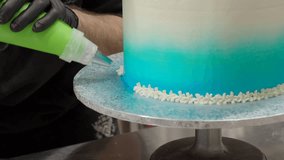 pastry chef cake designer decorating turquoise blue white frosted cheesecake in kitchen with piping bag 4k video