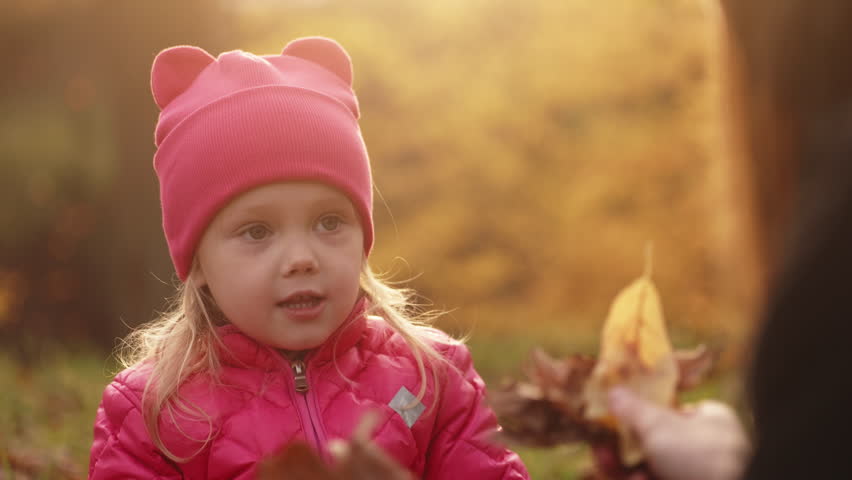 Mother and daughter having fun at autumn golden forest, toddler girl laughs. Real childs emotions, true happiness, nice sunny day out of the city, throwing up yellow and red leaves. High quality 4k 