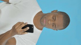 Vertical Video of Young African Man Talking on Phone on Blue Background