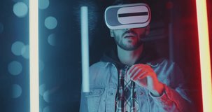 Slow motion portrait of young man wearing virtual reality glasses moving hands against neon lights background. Technology and future concept.