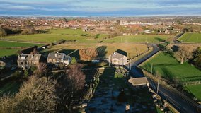 Aerial drone video footage of a small village church and church yard, with gravestones and warm sunlight. Hartshead Moor, West Yorkshire, UK